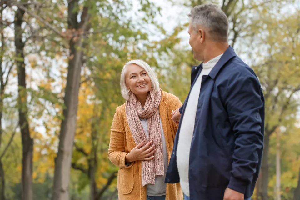 An older couple walking arm in arm through a park in the fall